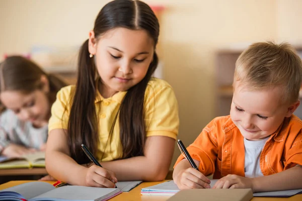 Montessori okulunda ders sırasında çok ırklı çocuklar fotokopi kitapları yazıyor.