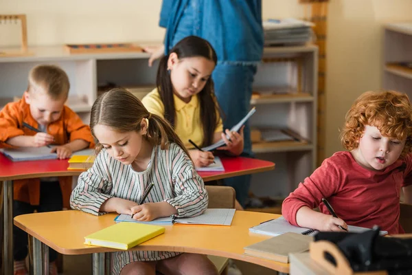 Multiethnic Children Writing Notebooks Teacher Blurred Background — Stock Photo, Image