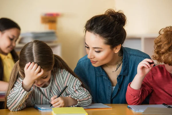 レッスン中にノートを書く少女を見ている若い先生 — ストック写真