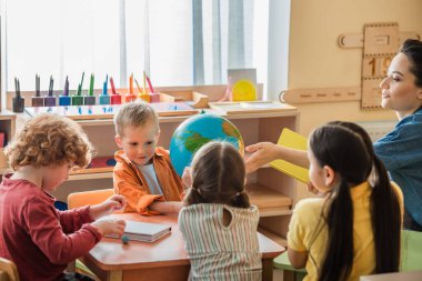 Öğretmen Montessori okulunda ders sırasında çocuklarla konuşurken dünyayı işaret ediyor.