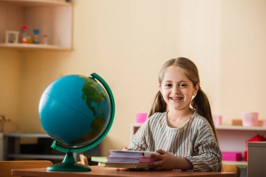 Montessori okulunda elinde kitaplarla oturan mutlu bir çocuk.