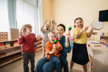 Montessori okulunda müzik enstrümanları çalan genç öğretmenli neşeli ırklar arası çocuklar.
