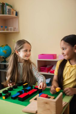 Montessori okulunda tahta bloklarla oynarken birbirine bakan mutlu ırklar arası kızlar.