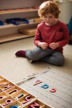 Montessori okulunda ahşap harflerin yanında oturan bulanık çocuk.