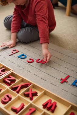 Montessori okulunda yerde ahşap harflerle oynayan çocuğun kısmi görüntüsü