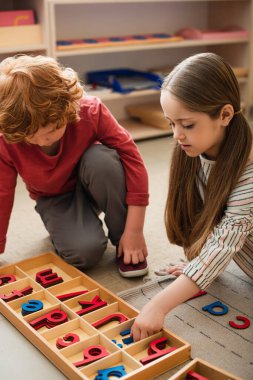 Montessori okulunda yerde tahta harflerle oynayan çocuklar.