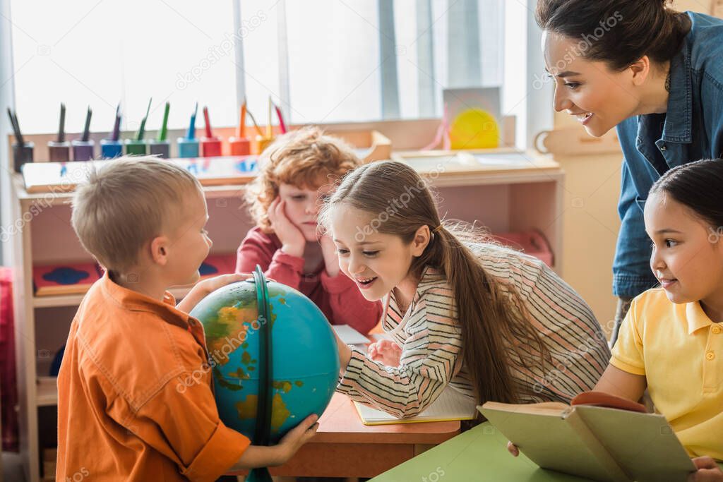 amazed girl looking at globe near interracial friends and teacher