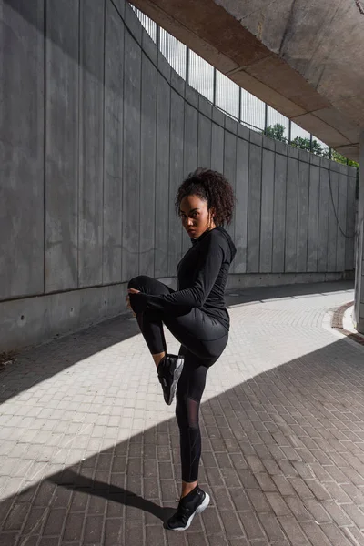 African american sportswoman warming up on urban street