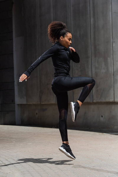 Боковой вид африканской женщины, прыгающей во время тренировки на городской улице 