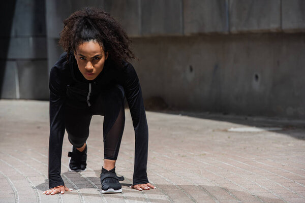 Young african american runner looking at camera while standing in starting pose outdoors 