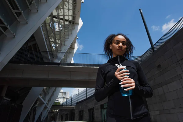 Vista Ángulo Bajo Deportista Afroamericana Auricular Sosteniendo Botella Deportiva Calle — Foto de Stock