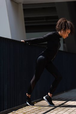 Kulaklıklı Afro-Amerikan sporcunun köprüde ısınma hareketleri. 