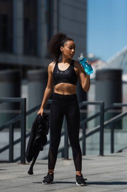 Açık havada spor şişesinde ceketi ve suyu tutan Afrikalı Amerikalı sporcu kadın. 