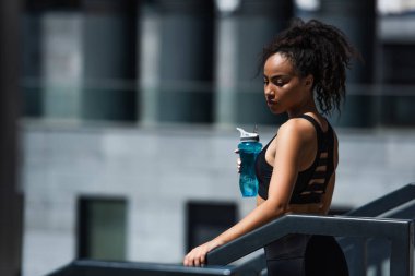 Siyah bluzlu Afro-Amerikan sporcu kadın elinde spor şişesi tutuyordu. 