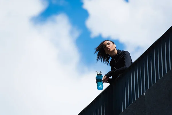 Vista Bajo Ángulo Deportista Afroamericana Sosteniendo Botella Deportes Con Cielo — Foto de Stock