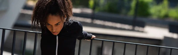 戴耳机的非裔美国女运动员在城市街道上暖身 高举横幅 — 图库照片