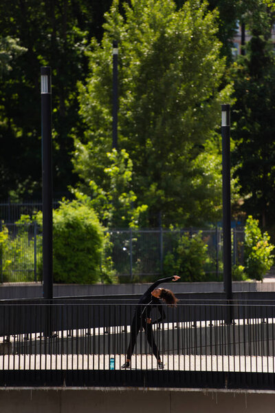 Young african american sportswoman bending while training on bridge 