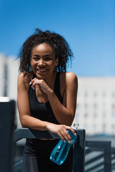 Alegre Deportista Afroamericana Sosteniendo Botella Deportiva Cerca Barandilla Calle — Foto de Stock