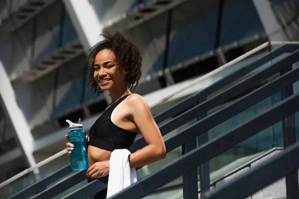 アフリカ系アメリカ人のスポーツ女性で タオルと水が屋外カメラで微笑む — ストック写真