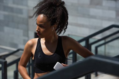 Kulaklıklı Afro-Amerikan sporcu kadın açık havada cep telefonu tutuyor. 