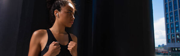 Африканская американская спортсменка в наушнике глядя в сторону на городской улице, баннер 