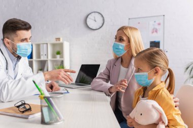 Tıbbi maskeli çocuk doktoru hastanedeki bir kadını işaret ediyor. 