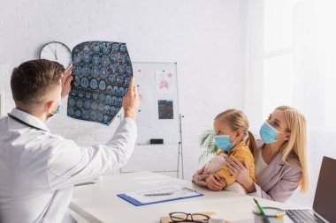 Klinikteki tıbbi maskeli anne ve kızının yanında MRI taraması yapan çocuk doktoru. 
