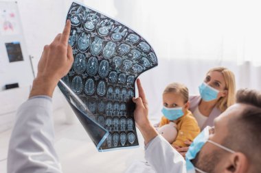 Tıbbi maskeli anne ve çocuğun yanında MRI taraması yapan bulanık çocuk doktoru. 
