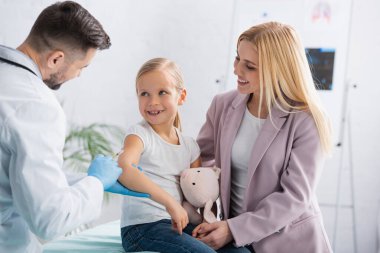 Gülümseyen ebeveyn aşı sırasında yanında şırıngayla doktora bakıyor. 