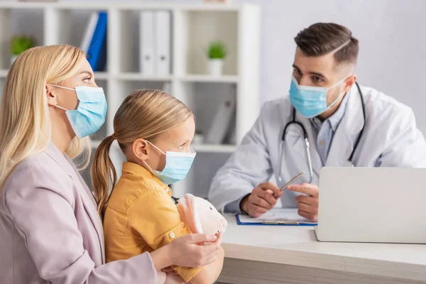 Mother Kid Medical Masks Sitting Blurred Doctor Laptop — Stock Photo, Image