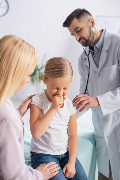 Kid sneezing near mother and doctor with stethoscope 
