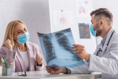 Koruyucu maskeli bir doktor, mutlu bir kadına ciğerlerinin röntgenini gösteriyor.
