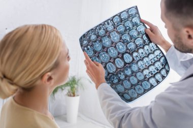 Doktor, bulanık ön planda klinikteki hastaya MRI taraması gösteriyor.