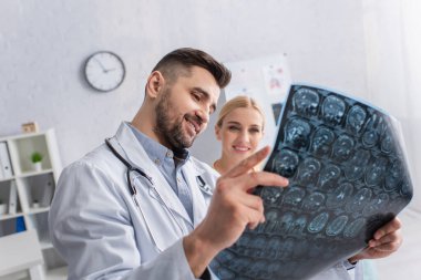 Gülümseyen doktor klinikteki mutlu kadına MRI taraması gösteriyor.