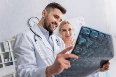 Neşeli kadın gülümseyen bir doktorun ellerinde MRI taramasına bakıyor.