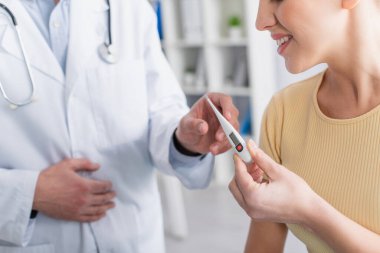 Klinikteki doktordan elektronik termometre alan gülümseyen kadının kısmi görüntüsü