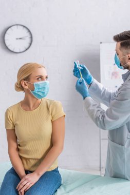 Koruyucu maskeli kadın şırıngayı aşıyla dolduran doktora bakıyor.