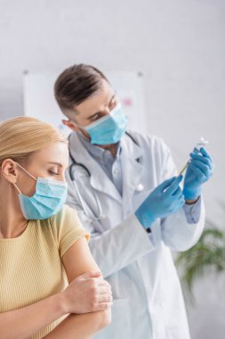 Doktor maskesindeki kadın şırıngayı aşıyla dolduruyor.