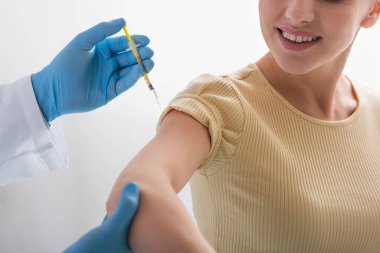 Kauçuk eldivenli doktorun gülümseyen kadına aşı enjekte etmesi.