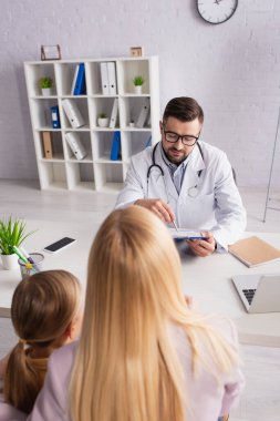 Hastanede anne ve kızının yanında dizüstü bilgisayara bakan çocuk doktoru.