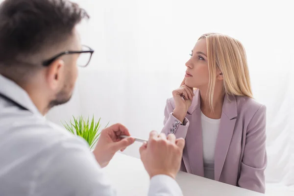 Blonde Vrouw Denken Buurt Wazig Arts Tijdens Afspraak Kliniek — Stockfoto