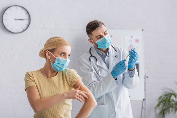 doctor in medical mask holding vaccine near woman in hospital
