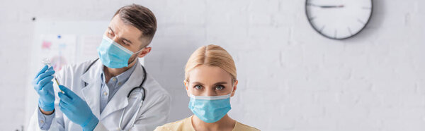 woman in medical mask looking at camera while doctor filling syringe with vaccine, banner