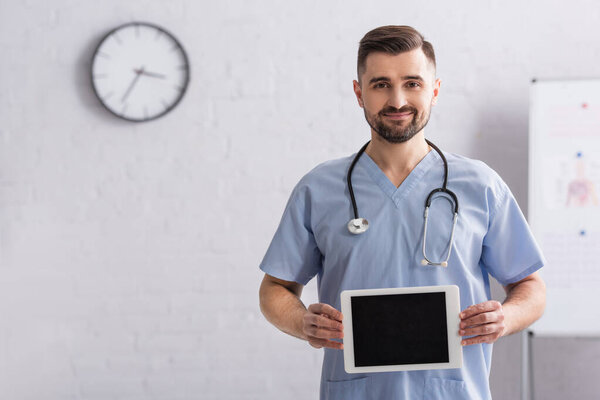 pleased doctor in blue uniform holding digital tablet with blank screen