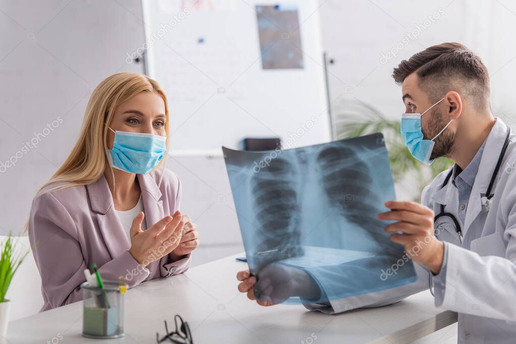doctor in medical mask showing lungs x-ray to positive woman during consultation