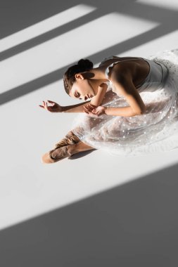 Yüksek açılı balerin manzaralı, gözleri kapalı, gri arka planda, güneş ışığıyla dans ediyor.