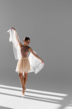 Güzel balerin bej etekli Gri arkaplanda güneş ışığıyla dans eden