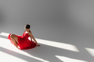 Kırmızı elbiseli balerin gri arka planda, güneş ışığıyla dans ediyor.