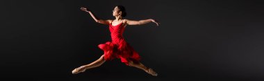 Side view of ballerina in pointe shoes and red dress jumping isolated on black, banner  clipart