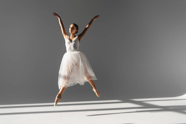 Молодая балерина танцует и прыгает на сером фоне с солнечным светом